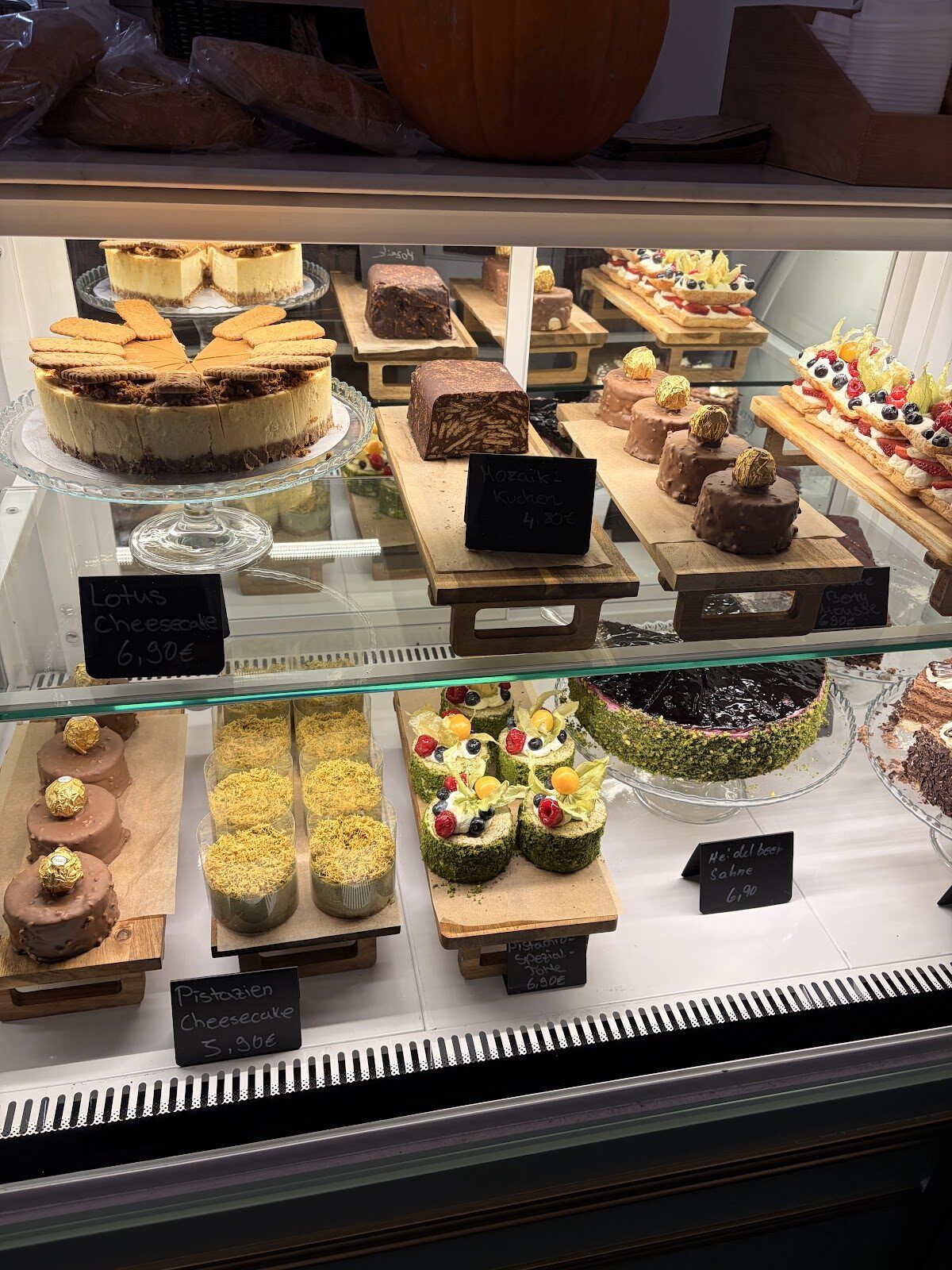 Kuchenvitrine bei Pistachio mit Cheesecakes, Mosaik-Kuchen und Törtchen auf Kreidetafel-Preisschildern